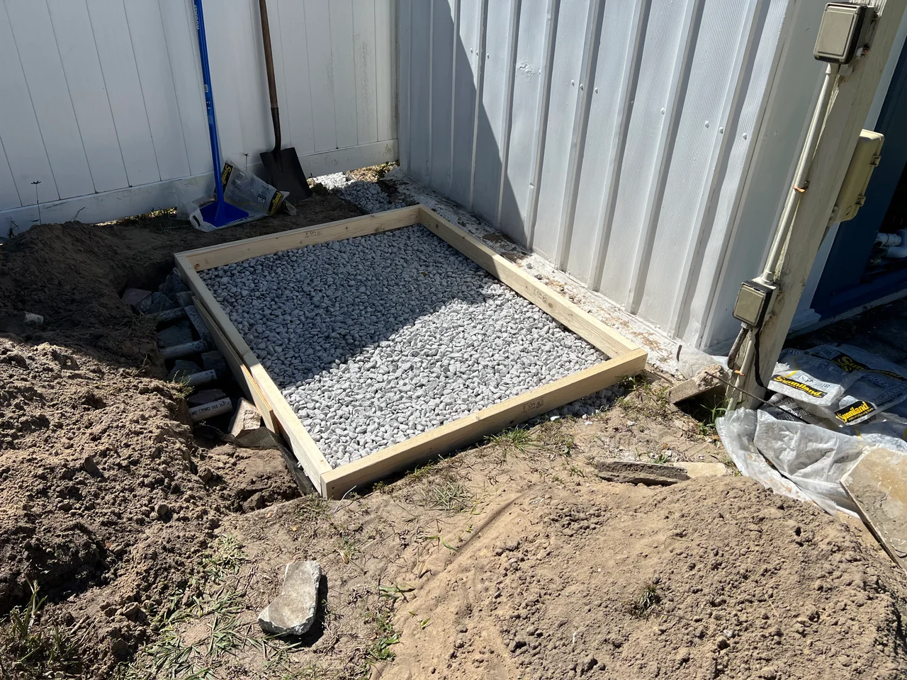 A timber form filled with gravel marks the foundation for the replacement pool equipment.