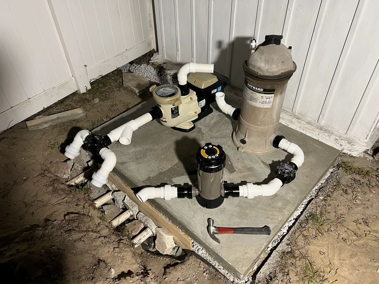 The replacement pump, filter and lengths of PVC plumbing arranged on the new concrete pad during assembly.