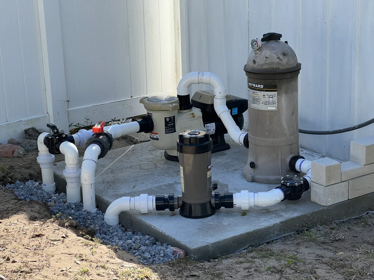The rebuilt pool pump setup with connected white PVC pipes, valves and filter on the concrete pad.